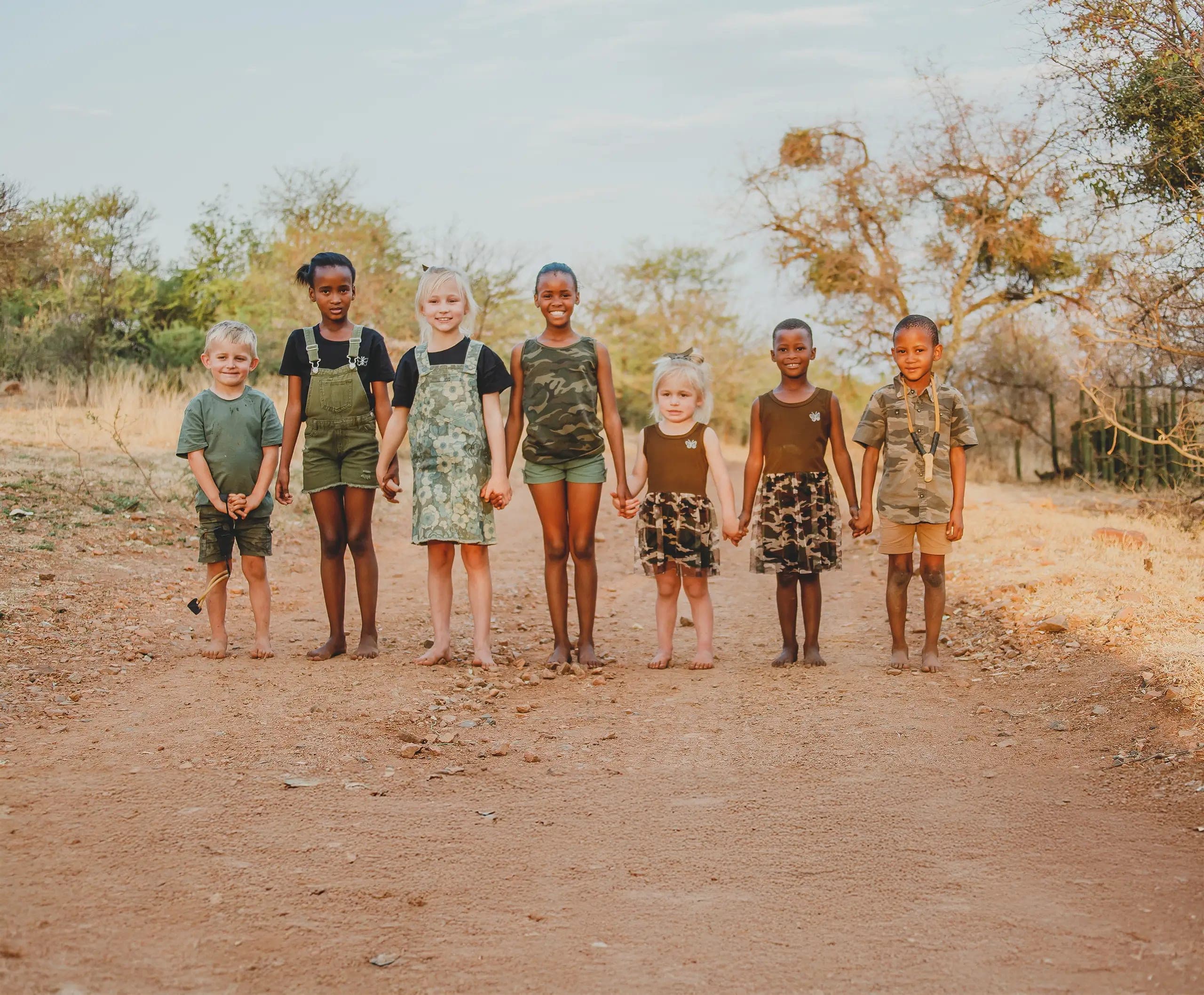 Seven children holding hands on a dirt road in the bush