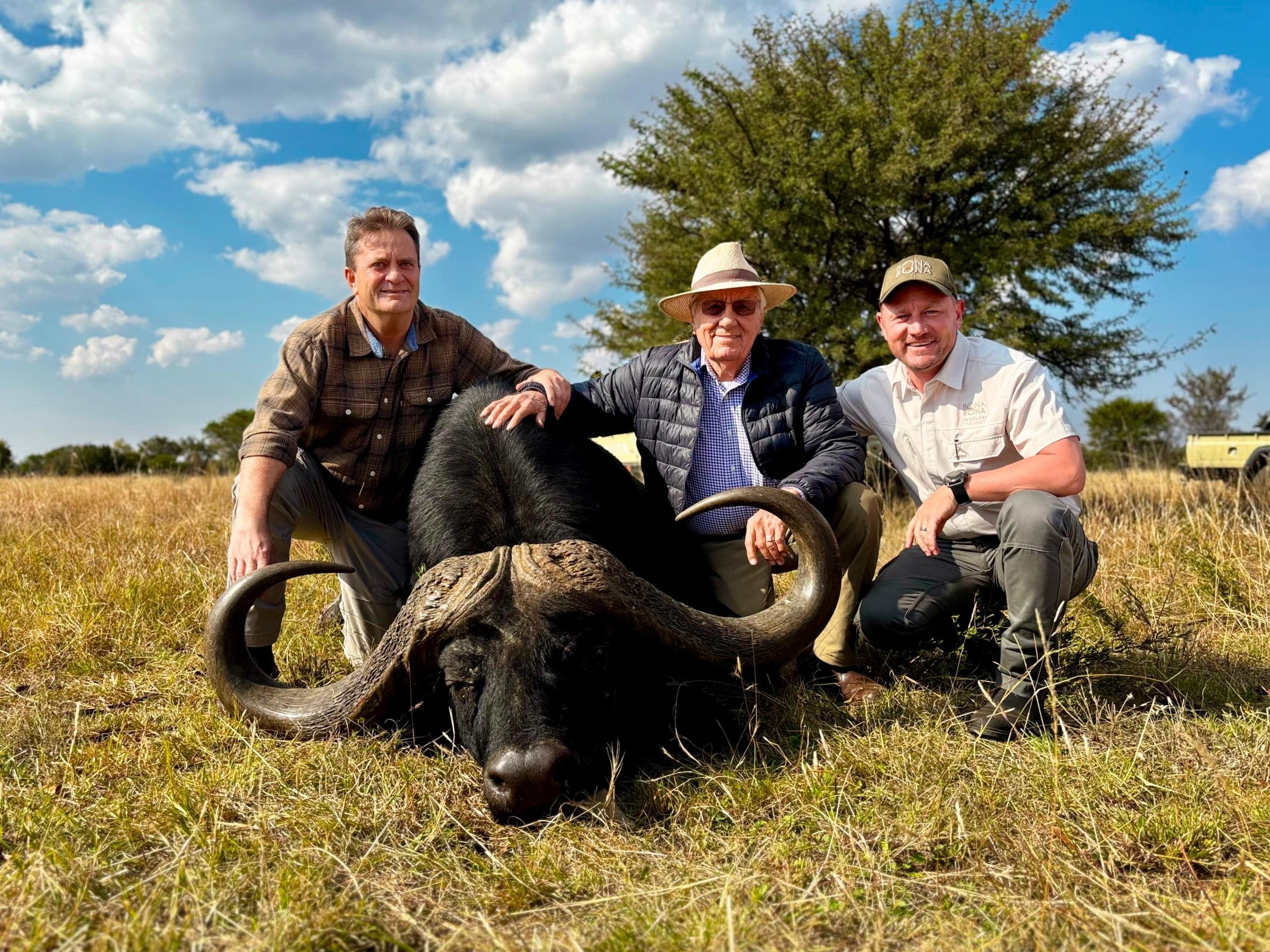 Three men kneeling in the veld behind a buffalo bull