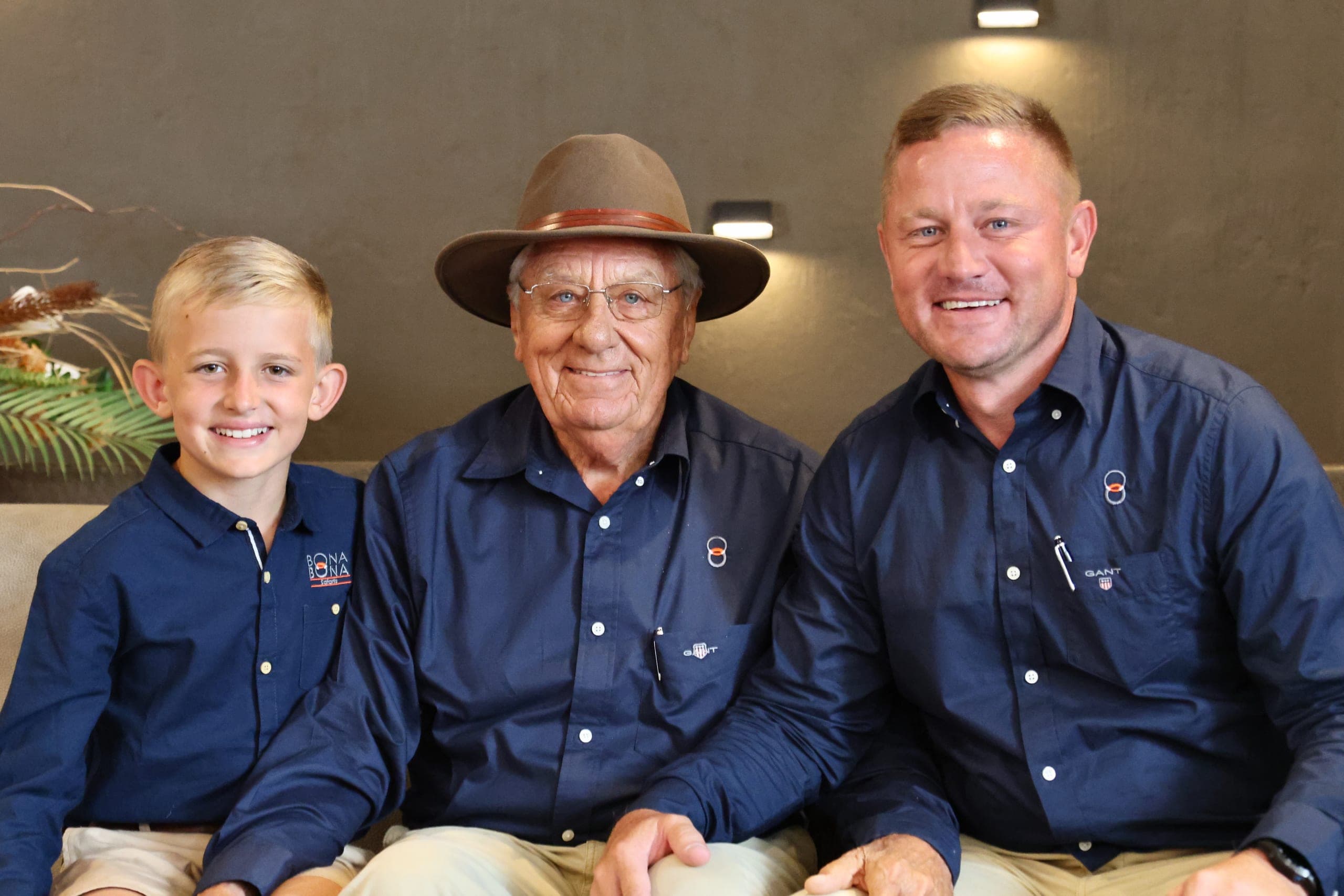 A boy, an older man in a hat and a younger man, smiling side by side at a Platinum Auction